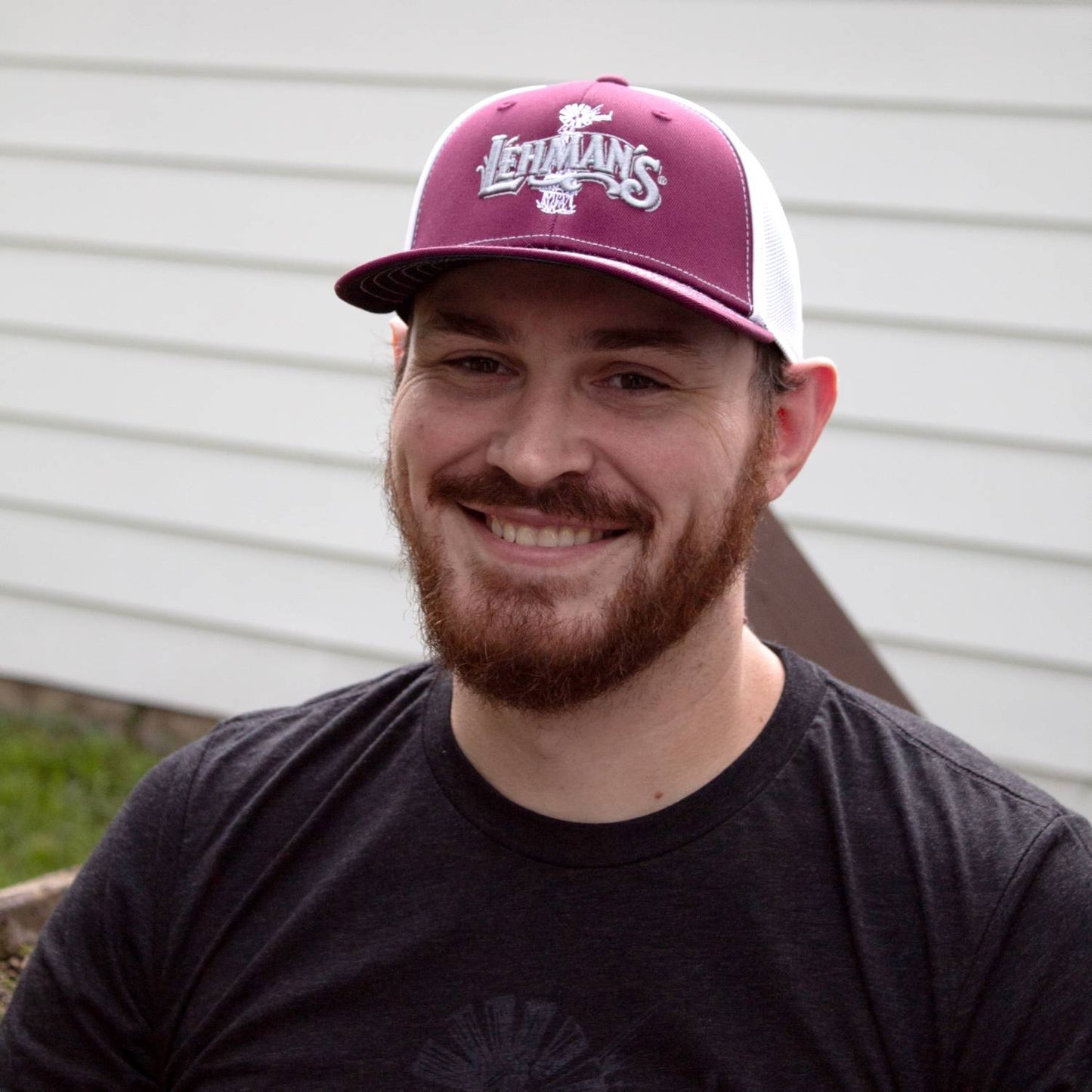 Smiling man wearing a handcrafted Lehman's embroidered trucker hat with a burgundy front panel, white stretch mesh back, and a slight pre-curved visor, featured in Health & Wellness, Clothing and Accessories, Best Sellers, and Promo Eligible collections.