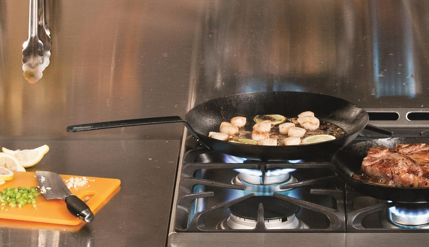 Black seasoned steel skillet with long handle cooking scallops on a gas stove burner, accompanied by a cutting board with chopped vegetables and lemon wedges, featured in Kitchen & Food, Cookware, Pots and Pans, USA Made, Best Sellers, and Promo Eligible collections.