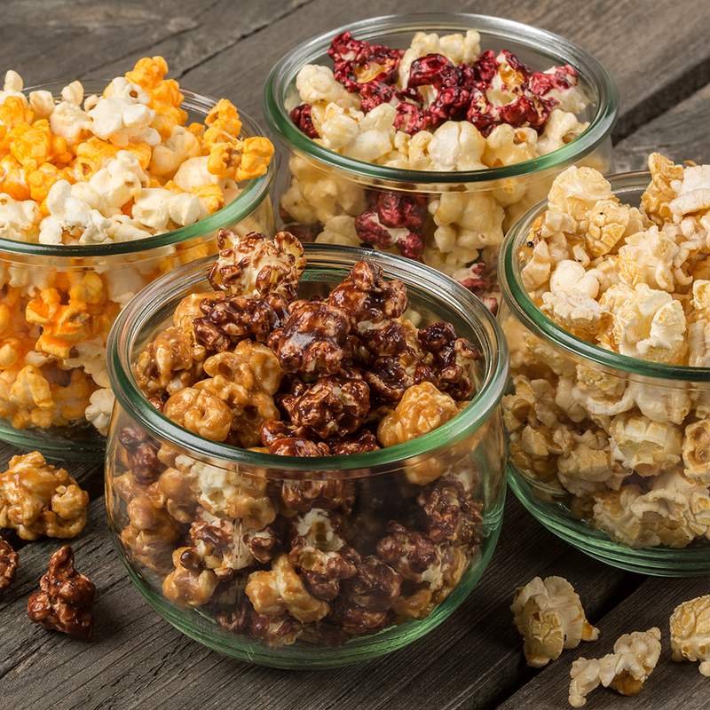 Four clear glass bowls filled with handcrafted popcorn in a variety of sweet and savory flavors, featuring rich chocolate, cheddar, caramel, and berry-coated pieces, made in USA, ideal for Kitchen & Food, Snacks and Sweets, Popcorn, USA Made, Best Sellers, and Promo Eligible collections.