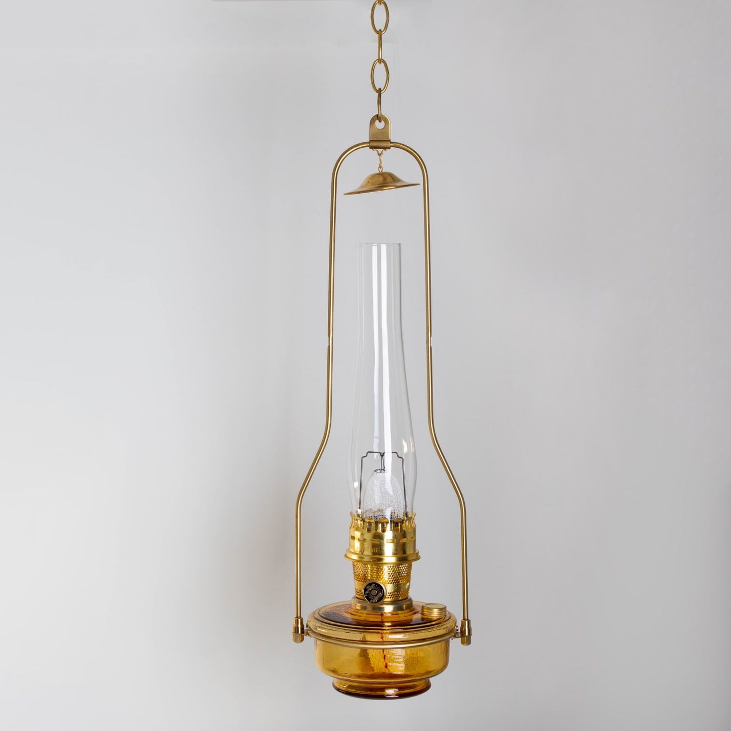 Handcrafted amber glass hanging oil lamp with gleaming brass frame and chain, designed for farm, garden, and emergency lighting, featured in best sellers and hanging lamps collections.