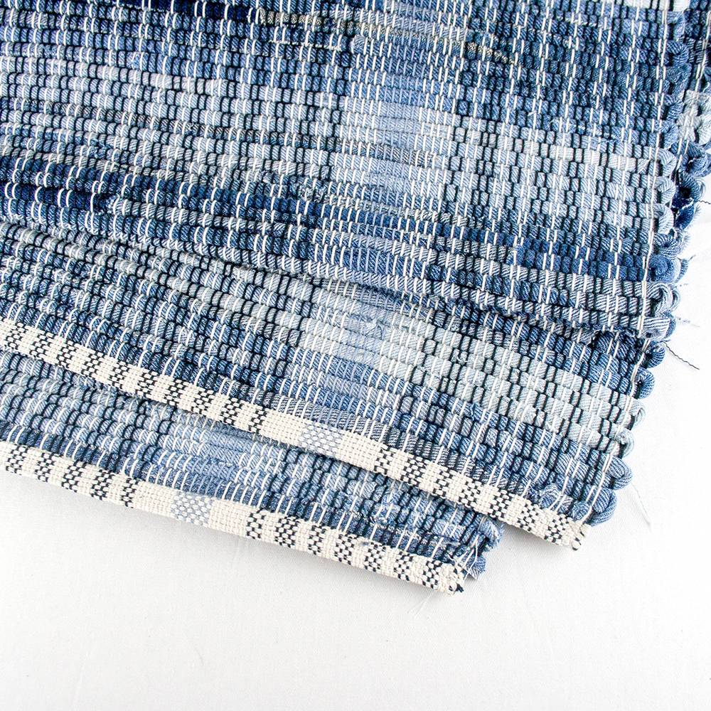 Close-up of a handcrafted woven denim rug with a textured blue pattern and finished edge, made in the USA, featured in Home & Decor and Best Sellers collections.