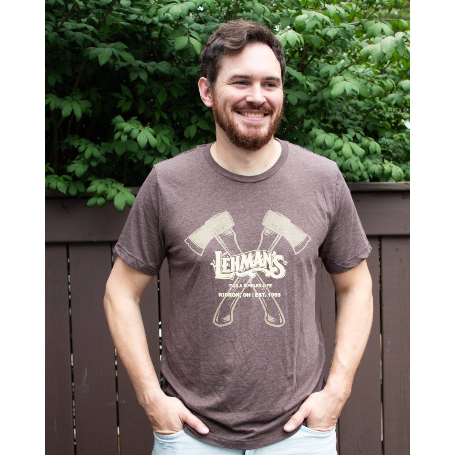 Man smiling outdoors wearing a soft brown lightweight t-shirt with cream crossed axes graphic and vintage text, ideal for Health & Wellness, Clothing and Accessories, and Best Sellers collections.