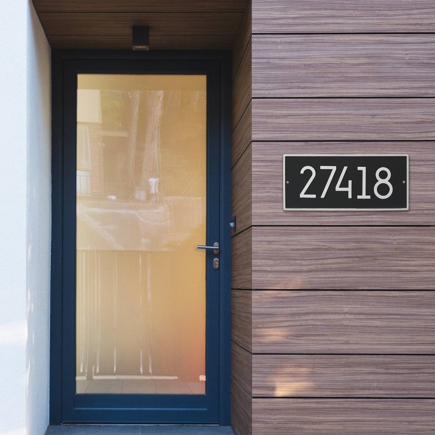 Handcrafted black and silver modern custom address plaque mounted on wood-paneled exterior wall next to a glass-panel front door, made in USA for Home & Decor and Mailboxes collections.