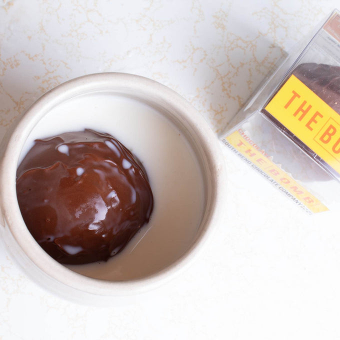 Handcrafted hot chocolate bomb with marshmallows melting in a white ceramic mug filled with warm milk, displayed beside clear packaging, ideal for Kitchen & Food, Snacks and Sweets, Beverages, USA Made, Best Sellers, and Promo Eligible collections.