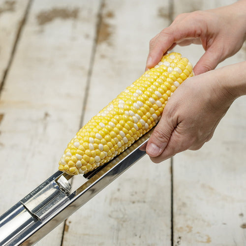 Hands holding an ear of corn being prepared with a stainless steel cutter designed for easy kernel removal, ideal for Kitchen & Food, Food Prep, and Choppers and Cutters collections.
