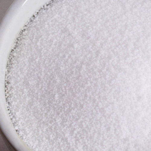 Close-up view of small, white, food-grade sodium hydroxide lye beads in a ceramic container, ideal for soapmaking and featured in Health & Wellness and Soapmaking Supplies collections.