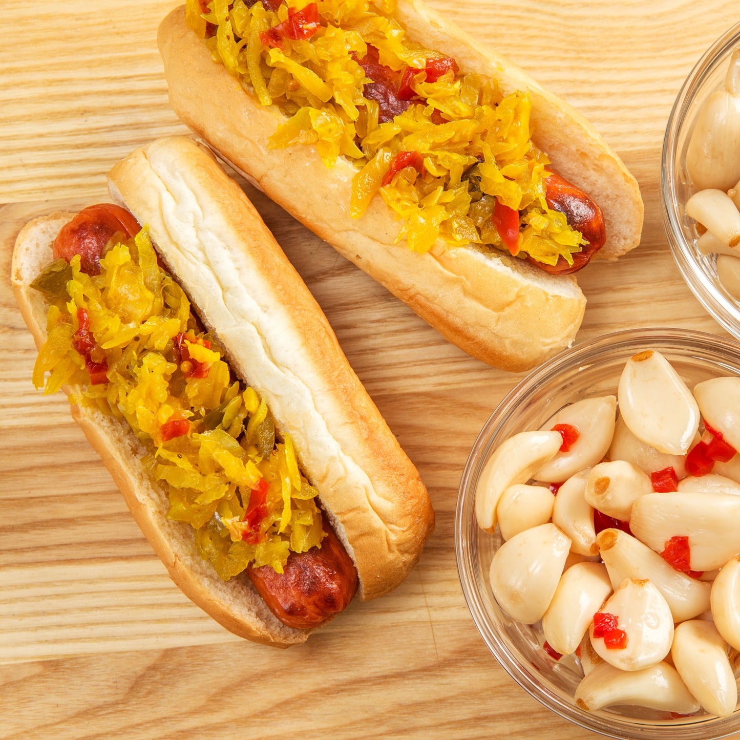 Two hot dogs topped with spicy Southern relish on a wooden surface, alongside a bowl of pickled garlic with red pepper, featured in Kitchen & Food, Pantry, USA Made collections.