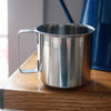 Stainless steel cup with a sturdy handle, placed on a wooden surface, ideal for camping, kitchen use, and outdoor dining in Farm, Garden & Tool, Kitchen & Food, and Camping collections.