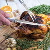 Handcrafted serrated steak knife with sharp surgical-grade stainless steel blade slicing a roasted whole chicken, surrounded by fresh herbs and citrus, ideal for Kitchen & Food and USA Made collections.