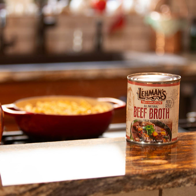 Can of Lehman's exclusive handcrafted beef broth placed on a rustic kitchen counter with a red pot cooking in the background, ideal for Farm, Garden & Tool, Kitchen & Food, Emergency Supplies, Food, Meats, Best Sellers, and Promo Eligible collections.