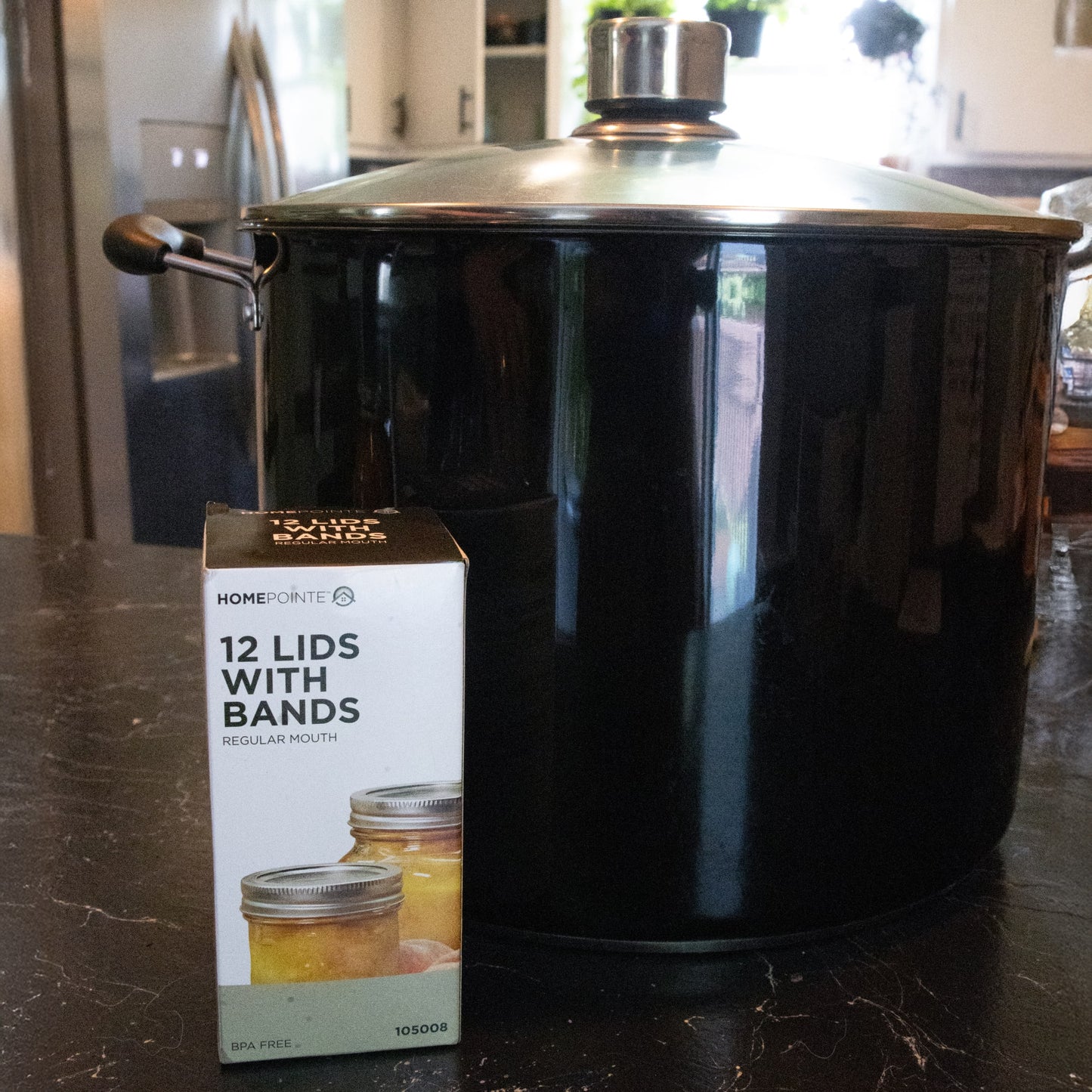 Box of 12 regular-mouth jar lids and bands with BPA-free sealing compound displayed in front of a large black cooking pot, ideal for Kitchen & Food and Food Preservation collections.