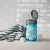 Blue glass jar with a hinged metal flip top lid, filled with cotton balls, displayed alongside a striped cloth and small mirror, featured in USA Made and Kitchen Accessories collections.