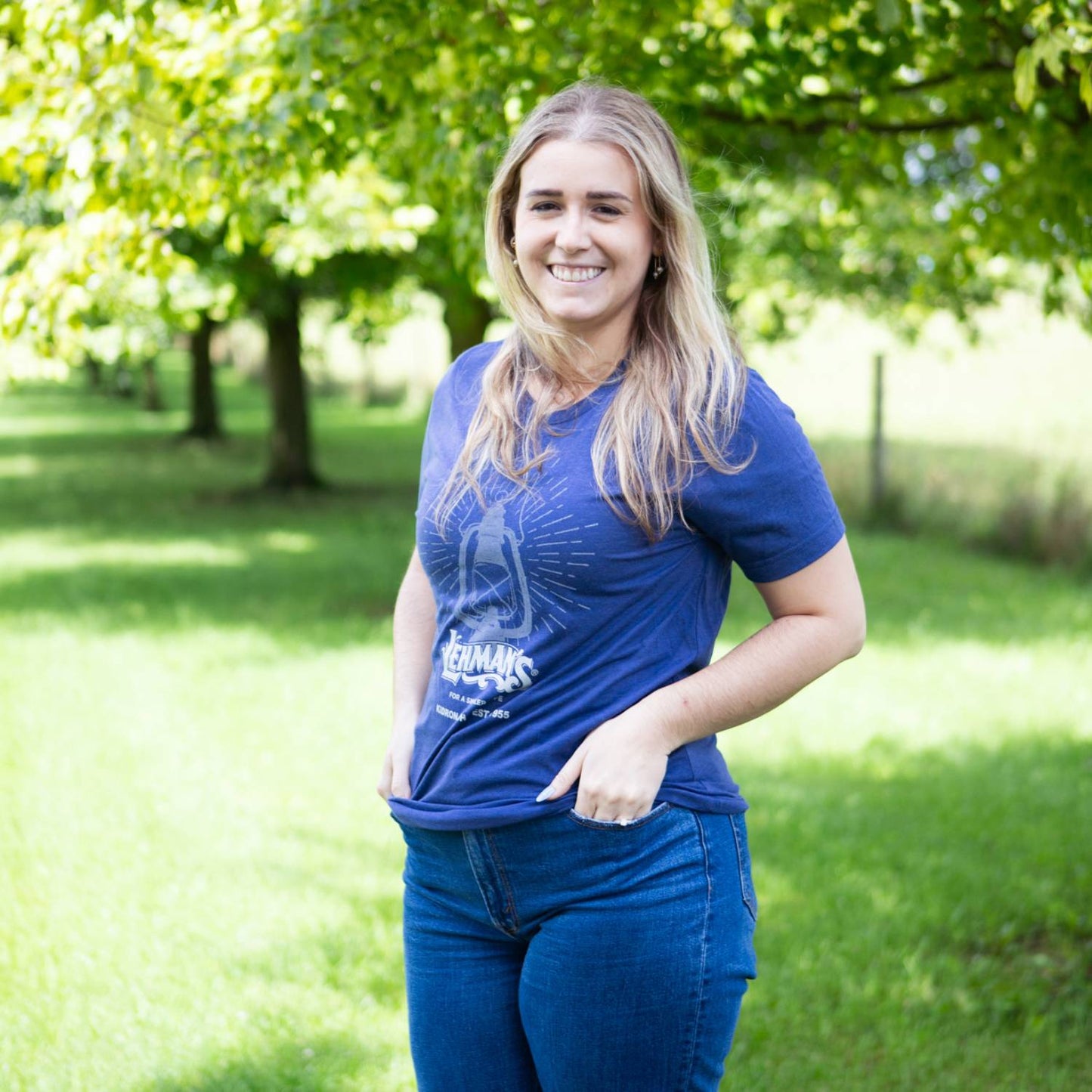 Smiling woman outdoors wearing a handcrafted blue comfy t-shirt with lantern graphic and white print, styled for Health & Wellness, Emergency Supplies, and Clothing collections.
