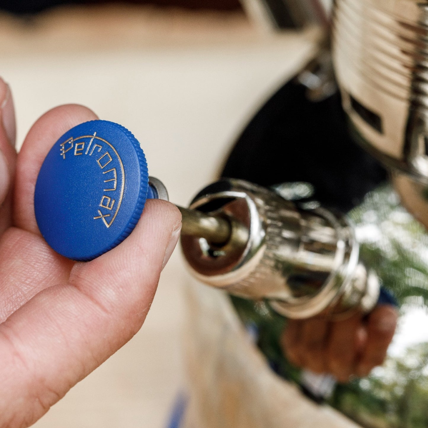 Hand turning a chrome pump with a blue knob engraved with Petromax logo, designed for use with lamps, featured in Lamps & Lighting, Parts and Accessories, Other Parts, Best Sellers, and Promo Eligible collections.