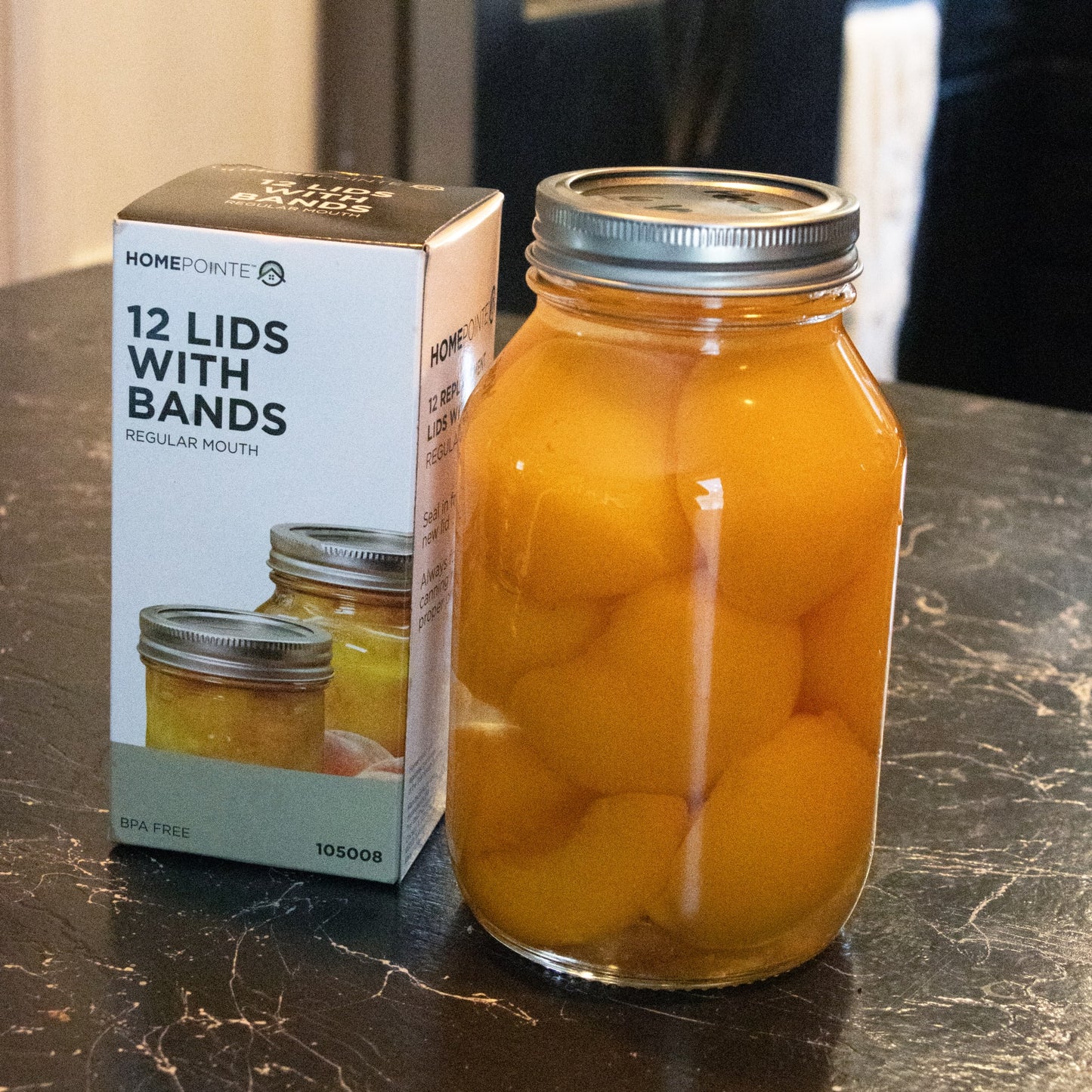 Box of 12 BPA-free regular-mouth canning jar lids and bands next to a glass jar filled with preserved peaches, perfect for Kitchen & Food and Food Preservation collections.