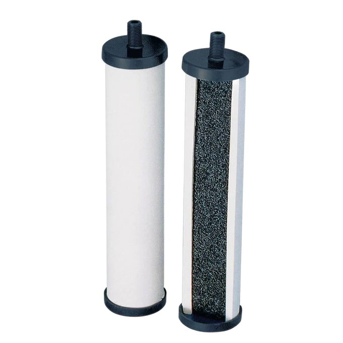 Two cylindrical replacement filtration elements for tabletop water filters, featuring black end caps and a white outer surface with one open side revealing granular filtering material inside.