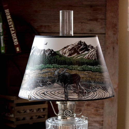 Clear oil lamp with brass burner and a parchment shade featuring a moose wading in water with forest and mountain landscape, ideal for Lamps & Lighting, Oil Lamps, Table Lamps, Best Sellers, Promo Eligible collections.