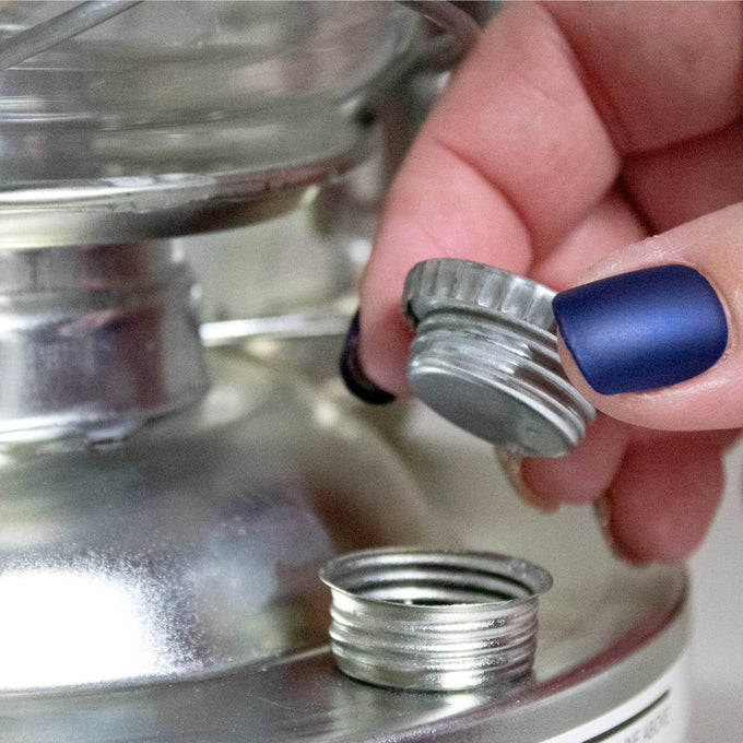 Hand holding the threaded metal fuel cap being unscrewed from a silver lantern fuel tank, highlighting durable construction for use in Camping, Emergency Supplies, and Farm, Garden & Tool collections.