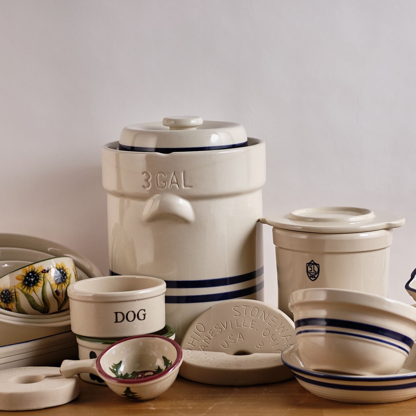 Assortment of handcrafted USA-made stoneware kitchen and food preservation crocks and bowls, including a large 3-gallon crock and smaller fermenting vessels with classic blue stripes.