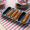 Seasoned cast iron cornstick pan with six golden-brown cornbread sticks, featuring dual handles and angled feet, ideal for Kitchen & Food, Cookware, Cast Iron, USA Made, and Best Sellers collections.