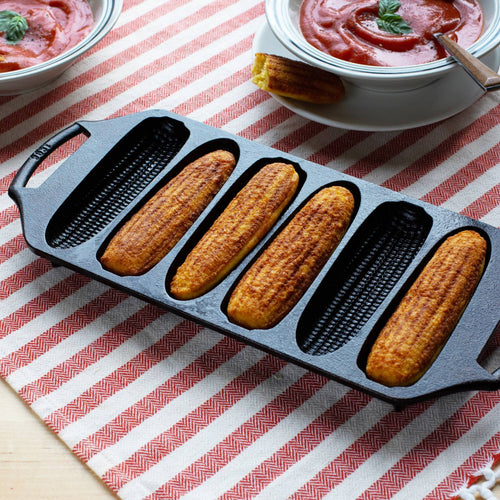 Seasoned cast iron cornstick pan with six golden-brown cornbread sticks, featuring dual handles and angled feet, ideal for Kitchen & Food, Cookware, Cast Iron, USA Made, and Best Sellers collections.