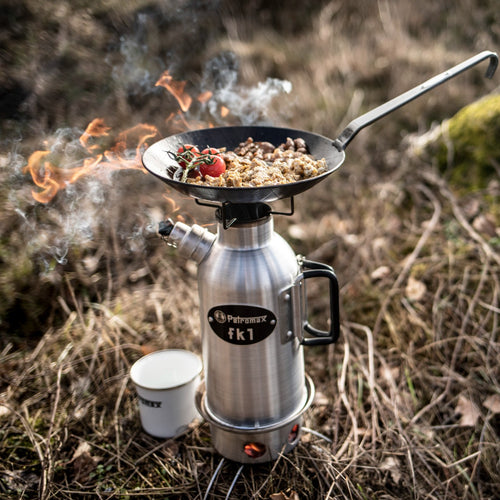 Outdoor camping stove setup with a compact stainless steel kettle and black frying pan cooking food with tomatoes over an open flame, featured in Kitchen & Food, Cookware, Cast Iron, and Best Sellers collections.