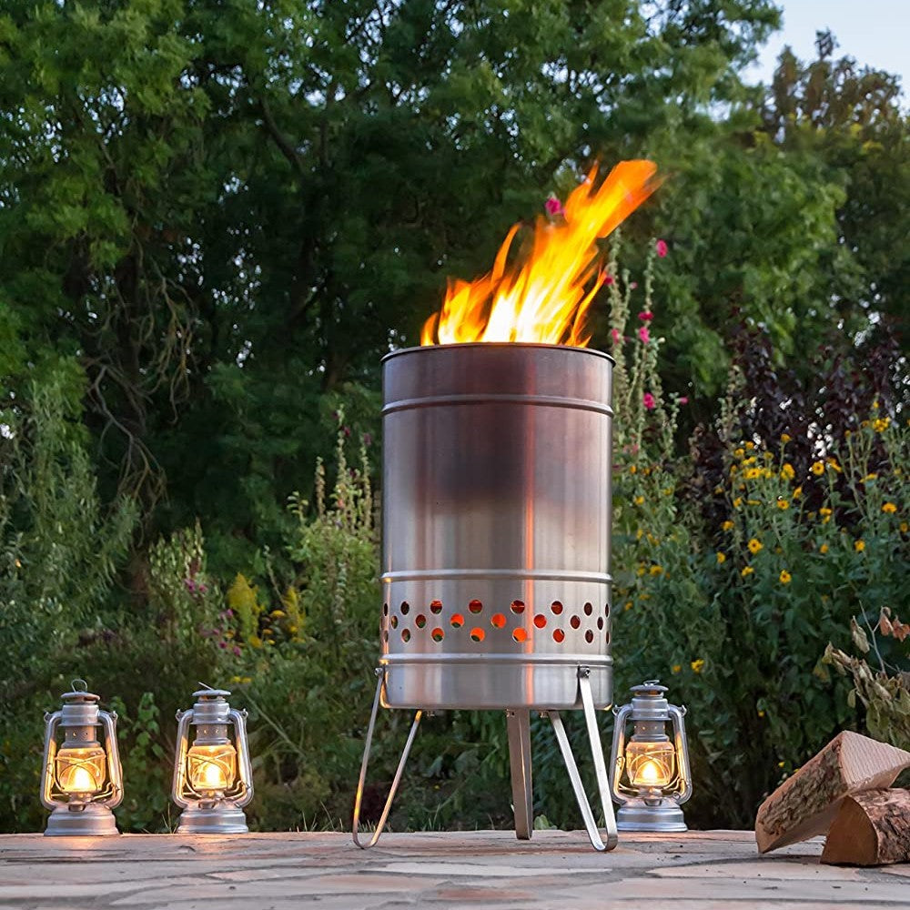 Brushed stainless steel fire barrel with perforated lower venting and sturdy legs, glowing warmly in an outdoor garden setting alongside four lit lanterns, ideal for Farm, Garden & Tool, Camping, and Best Sellers collections.