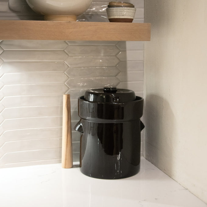 Handcrafted black stoneware fermenting crock with lid and natural wooden stomper on a white kitchen countertop, ideal for Kitchen & Food, Food Preservation, Fermenting and Pickling, Best Sellers, and Promo Eligible collections.