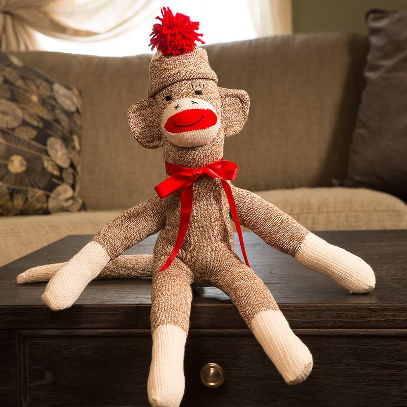 Hand-sewn sock monkey in brown and cream knit with red pom-pom hat and shiny red ribbon bow, handcrafted in USA, featured in Toys, Books & Games, USA Made, Children's Toys, Indoor Play, and Best Sellers collections.