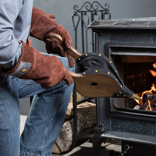 Handcrafted leather bellows with smooth stained pine wood handles and solid brass nozzle, made in USA, shown in use blowing air into a wood-burning stove, ideal for stoves and hearth accessories collections.