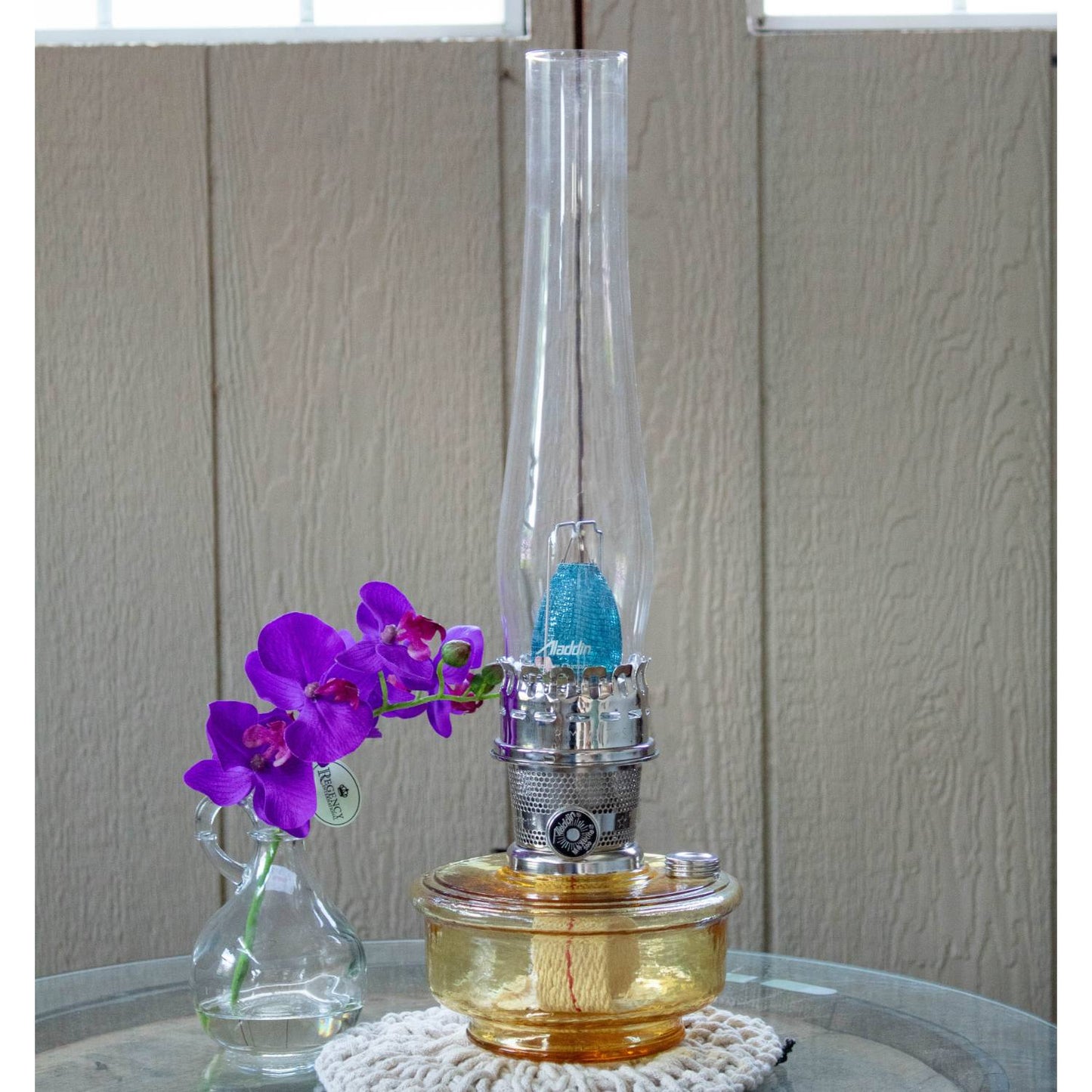 Handcrafted amber glass oil lamp with clear tall chimney and metal burner, displayed on a doily beside a small vase of purple flowers, perfect for Farm, Garden & Tool, Lamps & Lighting, Emergency Supplies, Oil Lamps, Wall Lamps, and Best Sellers collections.