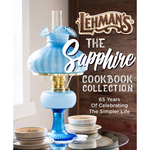 Blue vintage-style oil lamp with a ruffled glass shade placed beside stacks of bowls on a glass table, evoking a nostalgic, handcrafted USA-made lifestyle theme.