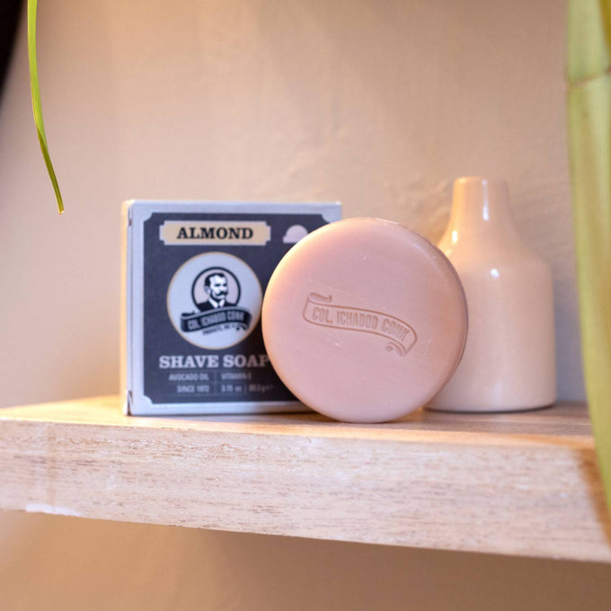 Handcrafted almond-scented shaving soap bar embossed with logo, resting beside its matching box on a wooden shelf, featuring nourishing ingredients, made in USA, part of Health & Wellness, Grooming and Personal Hygiene, Soaps and Soapmaking, USA Made, Best Sellers, and Promo Eligible collections.