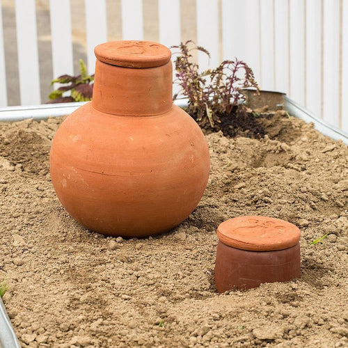 Two handcrafted unglazed terra cotta watering pots in natural clay buried in soil for slow, efficient irrigation of container gardens and small beds, featured in Farm, Garden & Tool and Garden Accessories collections.
