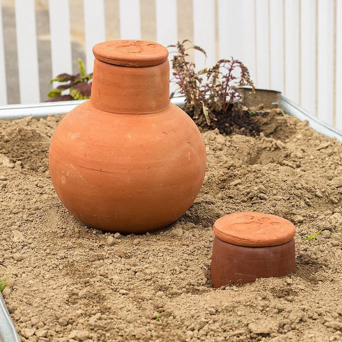 Two handcrafted unglazed terra cotta watering pots in natural clay buried in soil for slow, efficient irrigation of container gardens and small beds, featured in Farm, Garden & Tool and Garden Accessories collections.