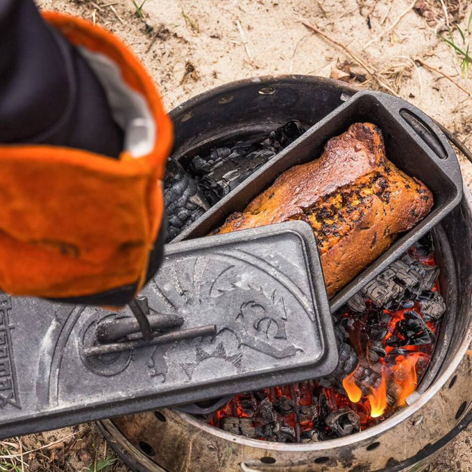 Cast iron loaf pan with embossed lid, shown baking bread over an outdoor fire pit, perfect for farm, garden, camping, kitchen, cookware, and bread making supplies collections.