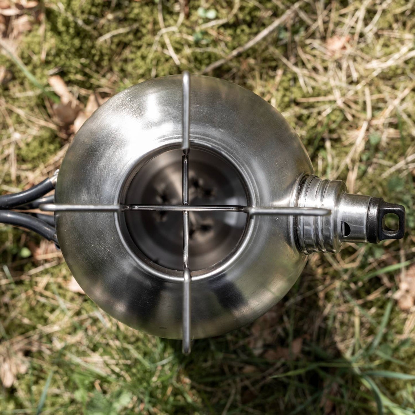 Top view of a handcrafted stainless steel fire kettle with sturdy handle and spout, resting on grass; ideal for farm, garden, camping, emergency supplies, and best seller collections.