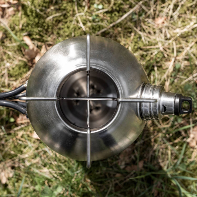 Top view of a handcrafted stainless steel fire kettle with sturdy handle and spout, resting on grass; ideal for farm, garden, camping, emergency supplies, and best seller collections.