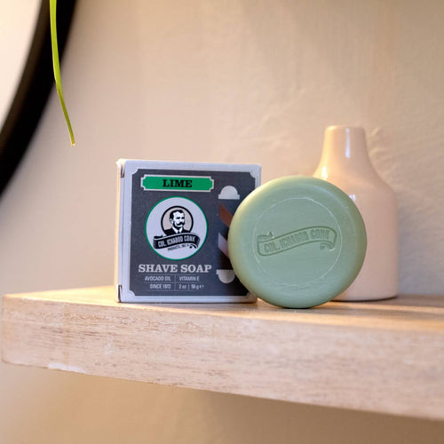 Round lime green shaving soap bar embossed with brand logo next to its boxed packaging, styled on a wooden shelf with neutral background, featured in Health & Wellness, Grooming and Personal Hygiene, Soaps and Soapmaking, USA Made, Best Sellers, Promo Eligible collections.