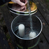 Hand filling a stainless steel gravity water filter with clear water, showing ceramic filter elements inside, suitable for camping, emergency supplies, and household use.