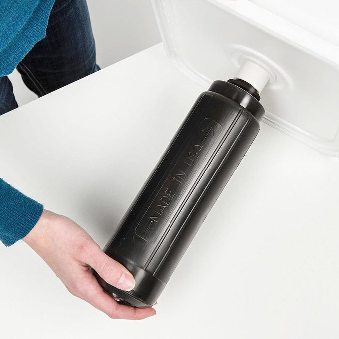 Hand inserting a black cylindrical water filter cartridge into a white plastic bucket, showcasing a handmade, durable filtration component for reliable water purification in farm, garden, and emergency use.