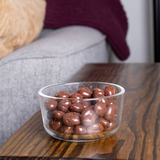 Clear glass bowl filled with smooth chocolate-covered raisins, displayed on a wooden table in a cozy setting, perfect for Kitchen & Food, Snacks and Sweets, and USA Made collections.