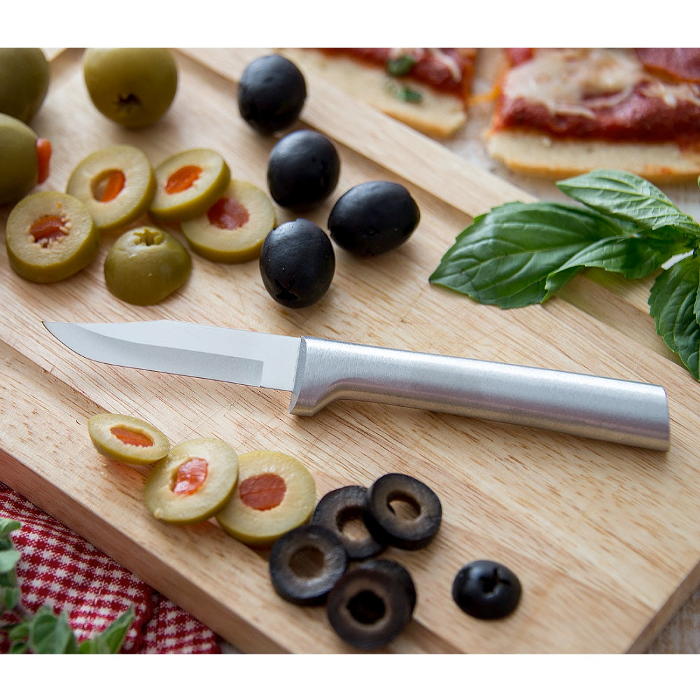 Sleek paring knife with a satin-finished cast aluminum handle and sharp carbon stainless steel blade resting on a wooden board with sliced olives, fresh basil, and pizza, ideal for kitchen and food prep in USA made collections.