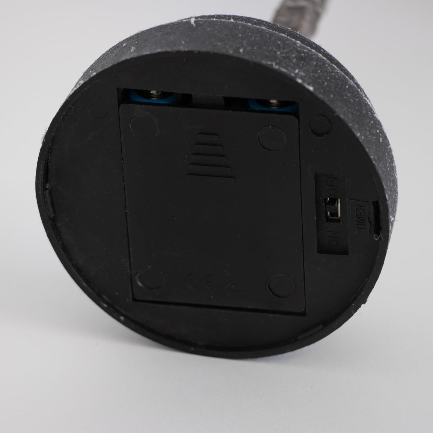 Bottom view of a black round battery compartment with a sliding cover and an on/off switch, part of a handcrafted decorative holiday item from Home & Decor, Holiday Decor, Best Sellers, and Promo Eligible collections.