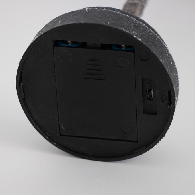 Bottom view of a black round battery compartment with a sliding cover and an on/off switch, part of a handcrafted decorative holiday item from Home & Decor, Holiday Decor, Best Sellers, and Promo Eligible collections.