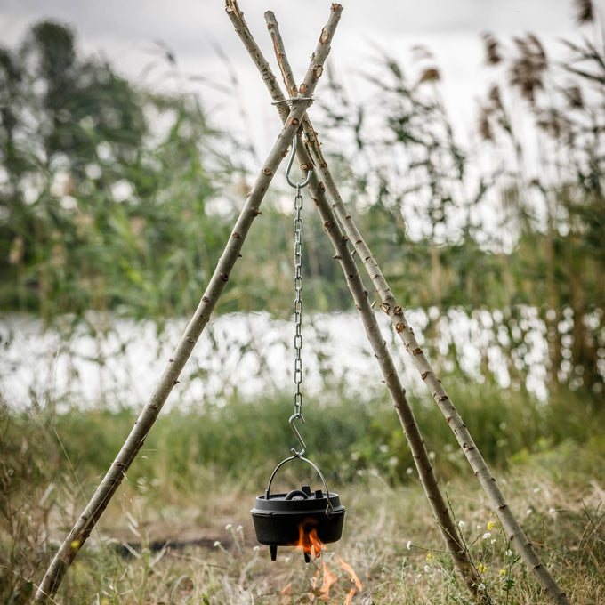 Sturdy outdoor tripod made from natural branches held by a stainless steel lashing set with hooks and chain, supporting a cooking pot over an open campfire in a grassy camping area, ideal for Farm, Garden & Tool, Camping, Best Sellers, and Promo Eligible collections.