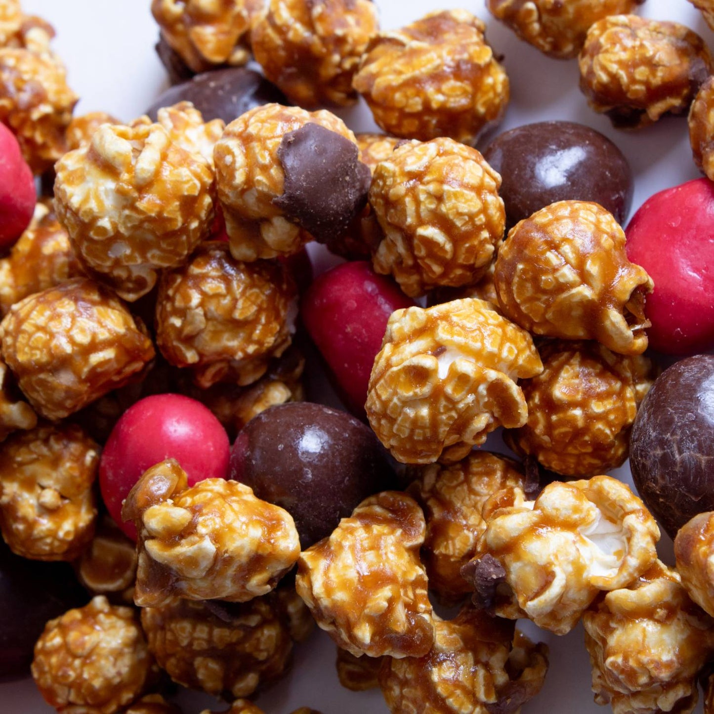 Close-up of handcrafted caramel popcorn blended with milk chocolate and festive red candy pieces, featured in Kitchen & Food, Snacks and Sweets, Popcorn, Best Sellers, and Promo Eligible collections.