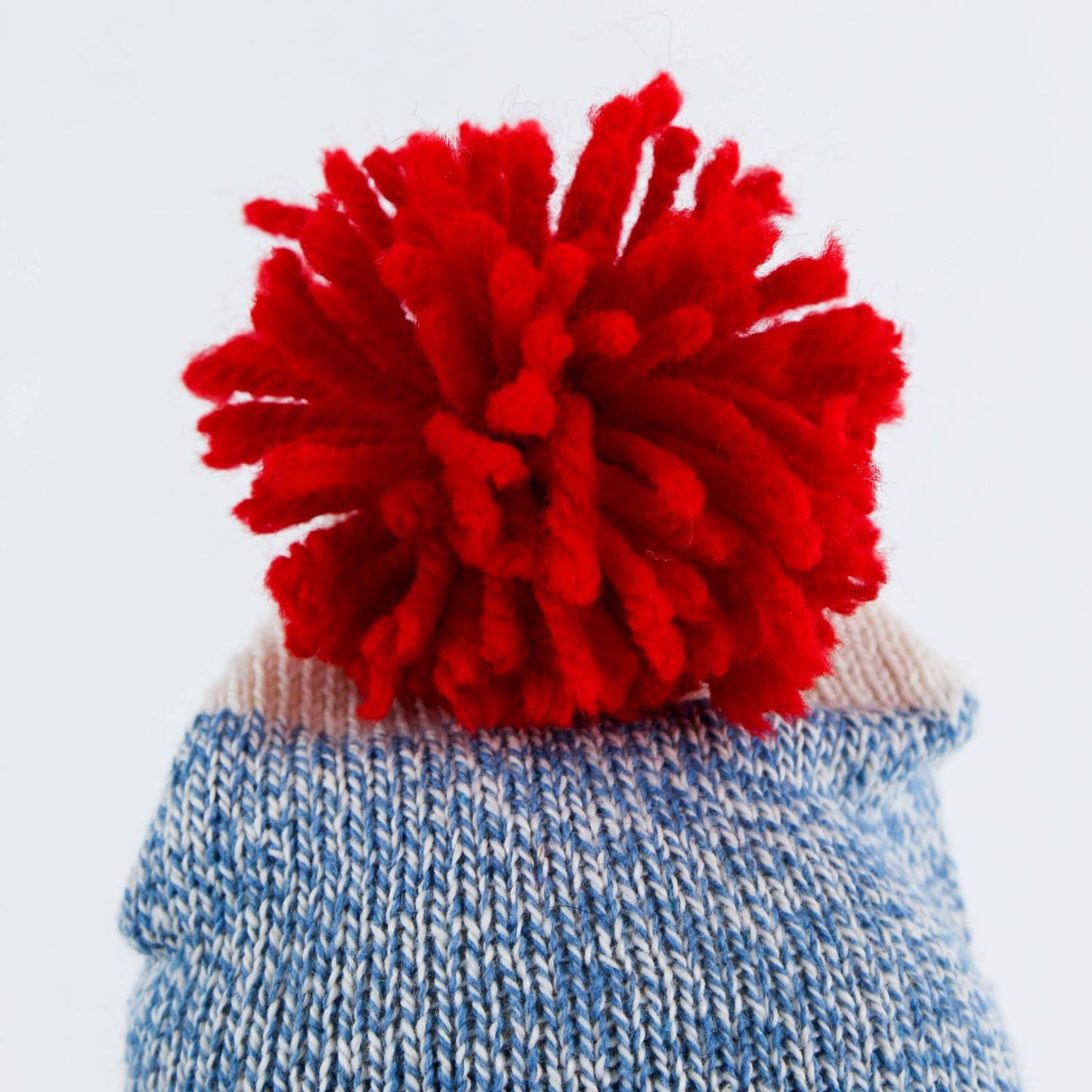Close-up of a hand-stitched blue knit hat topped with a bright red yarn pom-pom, handcrafted in the USA, featured in Toys, Books & Games, USA Made, Children's Toys, Indoor Play, Best Sellers, and Promo Eligible collections.