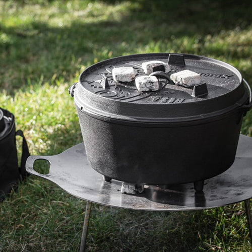 Robust cast iron Dutch oven with three legs heating outdoors on a metal stand, featuring a fitted embossed lid with charcoal briquettes for even cooking, perfect for Kitchen & Food, Cookware, Cast Iron, Best Sellers, Promo Eligible collections.