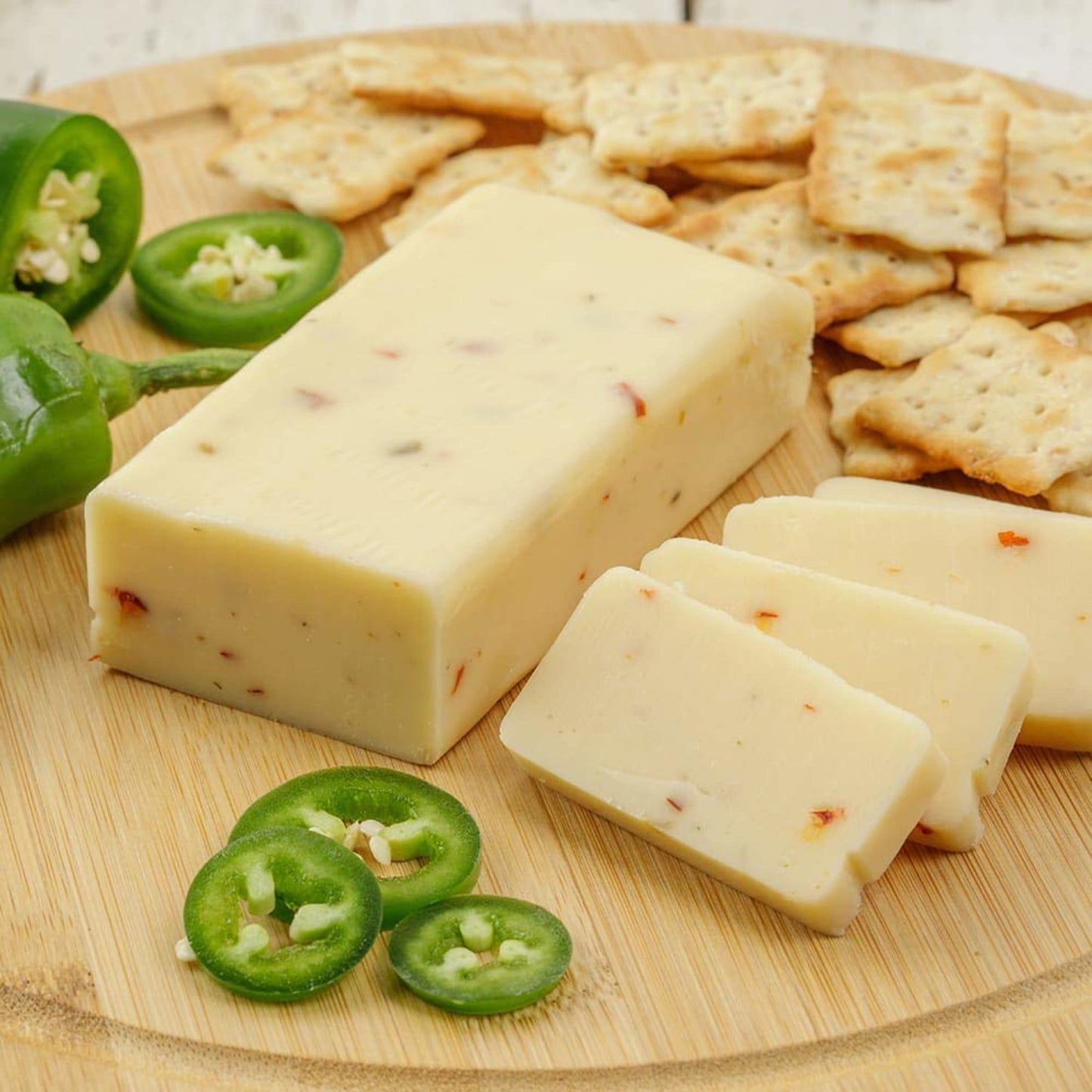Handcrafted shelf-stable cheese block infused with spicy pepper flakes, sliced and served on a wooden board with crackers and fresh jalapeño slices, ideal for Kitchen & Food, Snacks and Sweets, Pantry, USA Made, Best Sellers, and Promo Eligible collections.